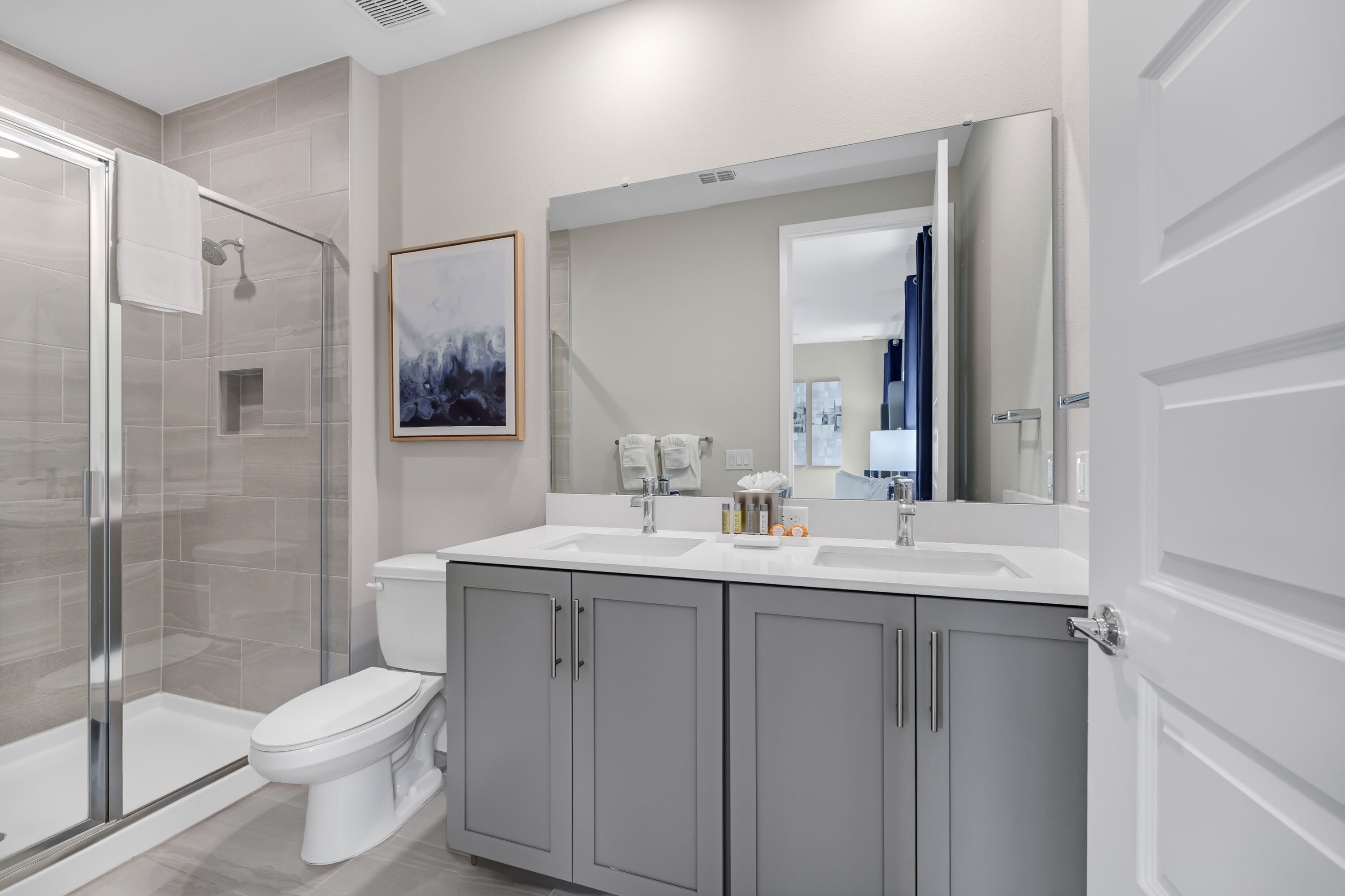 Un baño moderno con cabina de ducha de vidrio, inodoro blanco y tocador doble con alacenas.