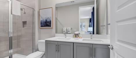 Un baño moderno con cabina de ducha de vidrio, inodoro blanco y tocador doble con alacenas.
