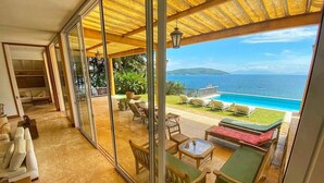 Ein geräumiger Balkon mit Glastür zum Poolbereich, Gartenmöbel und Blick aufs Meer.