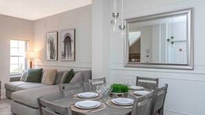 A dining area with a wooden table set for four, a grey sofa, and a large mirror on the wall. - Enjoy all the Theme Parks and what Orlando has to offer at Terra Verde Resort! (Kissimmee)