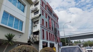 Un hotel de varios pisos con un cartel grande que dice 'HOTEL' en la fachada, ventanas amplias y un estacionamiento visible con coches.