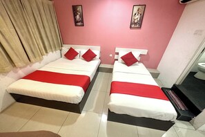 Une chambre d’hôtel avec deux lits, chacun agrémenté de draps blancs et rouges, un rideau beige et deux tableaux encadrés accrochés aux murs roses.