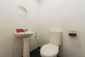 Une salle de bain avec des toilettes blanches, un lavabo sur colonne et un sèche-mains.