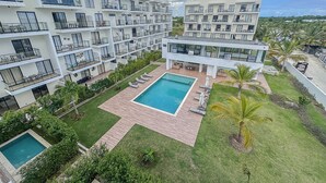 Ett modernt hotell med flera våningar, balkonger, en central pool och en vackert anlagd trädgård.