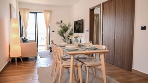 En matplats med ett träbord för fyra personer, omgiven av matchande stolar, en soffa och ett stort fönster med gardiner.