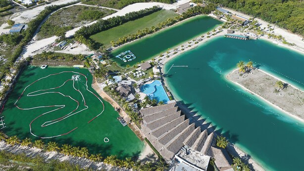 Ett flygbildsbild av ett semesterområde med flera pooler, en stor sandstrand och en småbåtshamn.