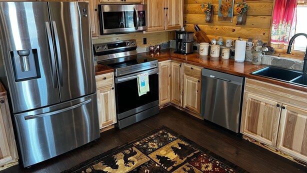 A modern kitchen with stainless steel appliances, wooden cabinets, and a stone backsplash. - Log Cabin in Whitehall (Whitehall)