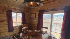 A cozy cabin interior with a wooden dining table set for four, surrounded by chairs, and a chandelier above. - Log Cabin in Whitehall (Whitehall)