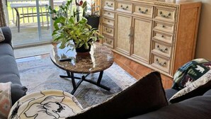 Una sala de estar con un sofá, una mesa de centro con una planta, un televisor sobre un mueble bajo, y un ventanal corredizo que da a un espacio exterior.