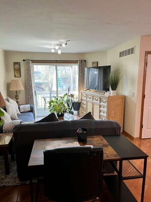 A living room with a sofa, a TV, a dining table with chairs, a ceiling fan, and a sliding glass door leading to an outdoor area.