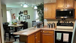 Una cocina con armarios de madera, microondas, horno, una mesa de comedor con sillas e iluminación colgante.