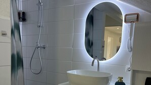 Ein modernes Badezimmer mit einem weißen Waschbecken, einem runden Spiegel, einer Handbrause und einem Handtuchhalter.