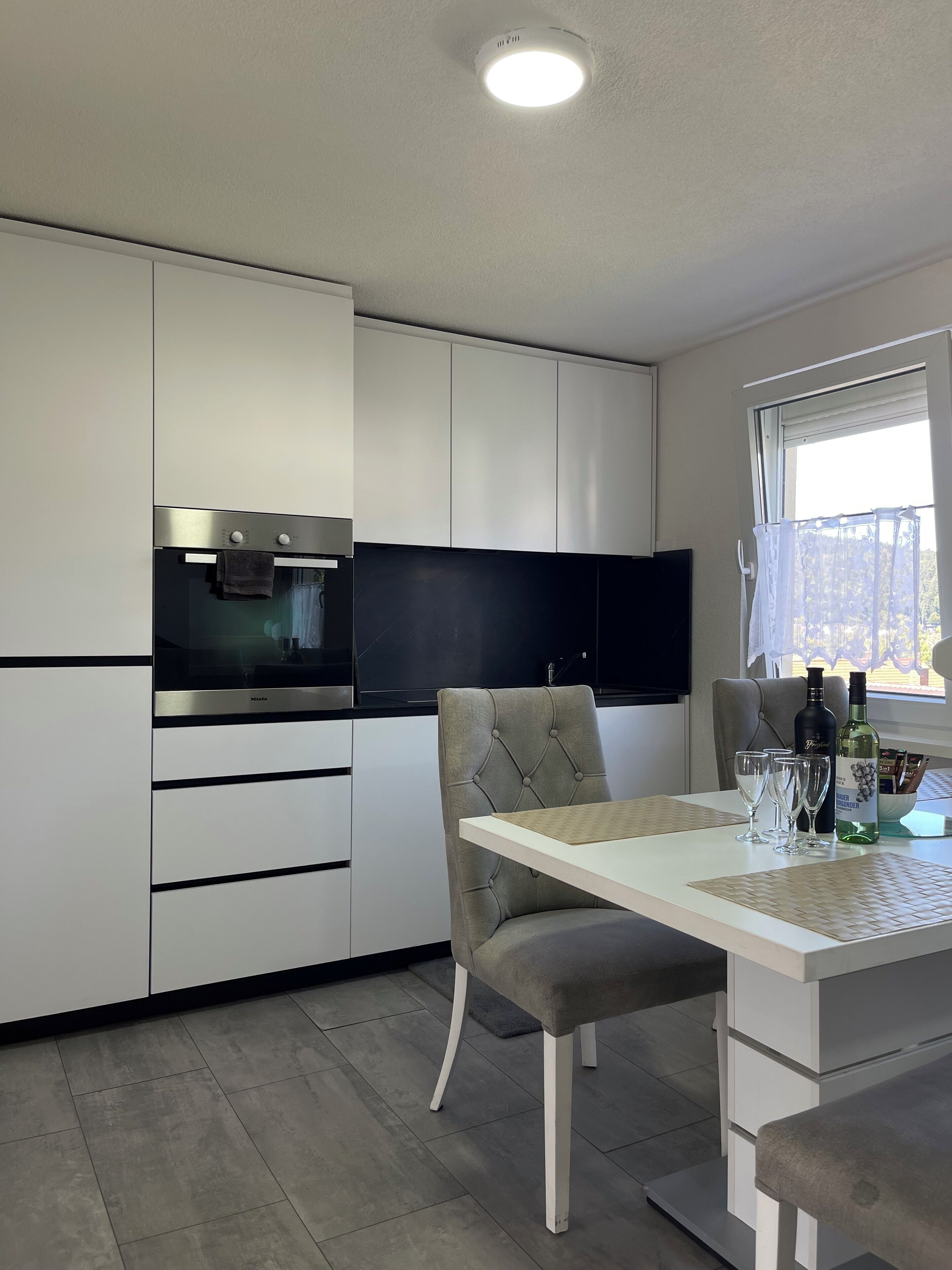 Een moderne keuken met witte kastjes, een inbouwoven en een eethoek met een tafel en stoelen.