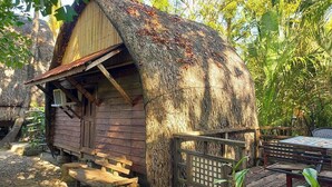 A rustic wooden cabin with a thatched roof, surrounded by lush greenery. - Surfer's Villa La Union By Zuzu (San Juan)