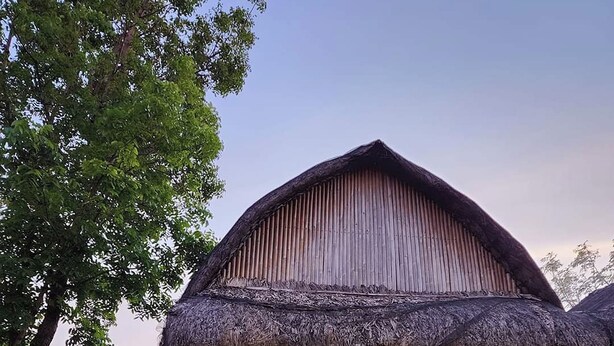 A rustic wooden house with a thatched roof, a wooden porch, and a wooden staircase leading to the entrance. - Surfer's Villa La Union By Zuzu (San Juan)