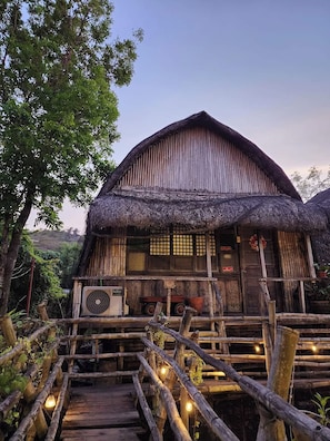 A rustic wooden house with a thatched roof, a wooden porch, and a wooden staircase leading to the entrance. - Surfer's Villa La Union By Zuzu (San Juan)
