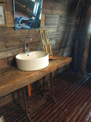Un baño rústico con lavamanos de madera y un grifo antiguo.