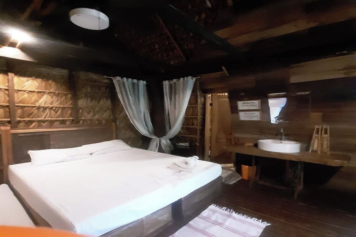 Una habitación tipo cabaña de madera con una cama, un banco de madera, un lavabo y un espejo.
