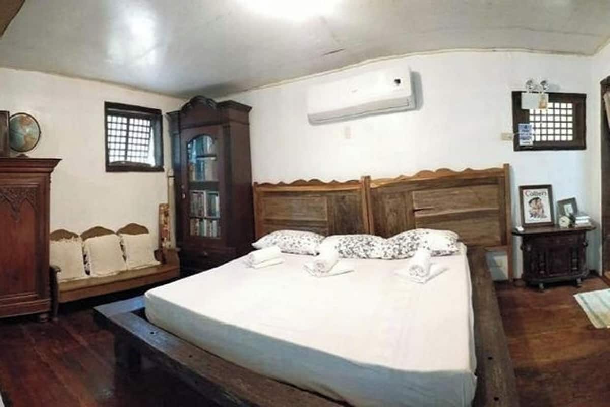 A bedroom with a wooden bed, a nightstand, a dresser, and a window with a grid pattern.