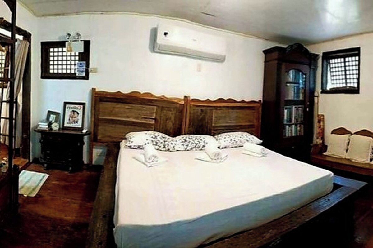 Un dormitorio con una cama de madera, una mesita de noche, un aparador y una ventana con barrotes.