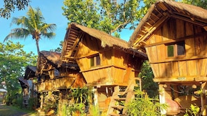 Wooden houses with thatched roofs, surrounded by lush greenery and palm trees. - Surfer's Villa La Union By Zuzu (San Juan)