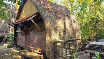 Una cabaña de madera rústica con techo de paja, rodeada de exuberante follaje.