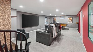 A modern home entertainment room with a large flat-screen TV, comfortable seating, and a pool table.