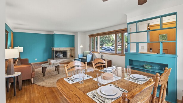 A dining area with a wooden table set for four, a fireplace, and a view of the outdoors through large windows.
