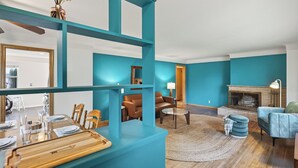 A modern living room with teal walls, a fireplace, and a dining area with a wooden table and chairs.