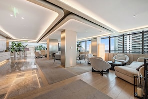 Un hall dâentrĂ©e spacieux au design moderne, comprenant un comptoir dâaccueil, un espace salon et de grandes fenĂȘtres offrant une vue sur la ville.