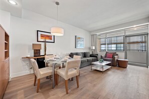 Un salon moderne avec un coin repas, un canapé gris et de grandes fenêtres.