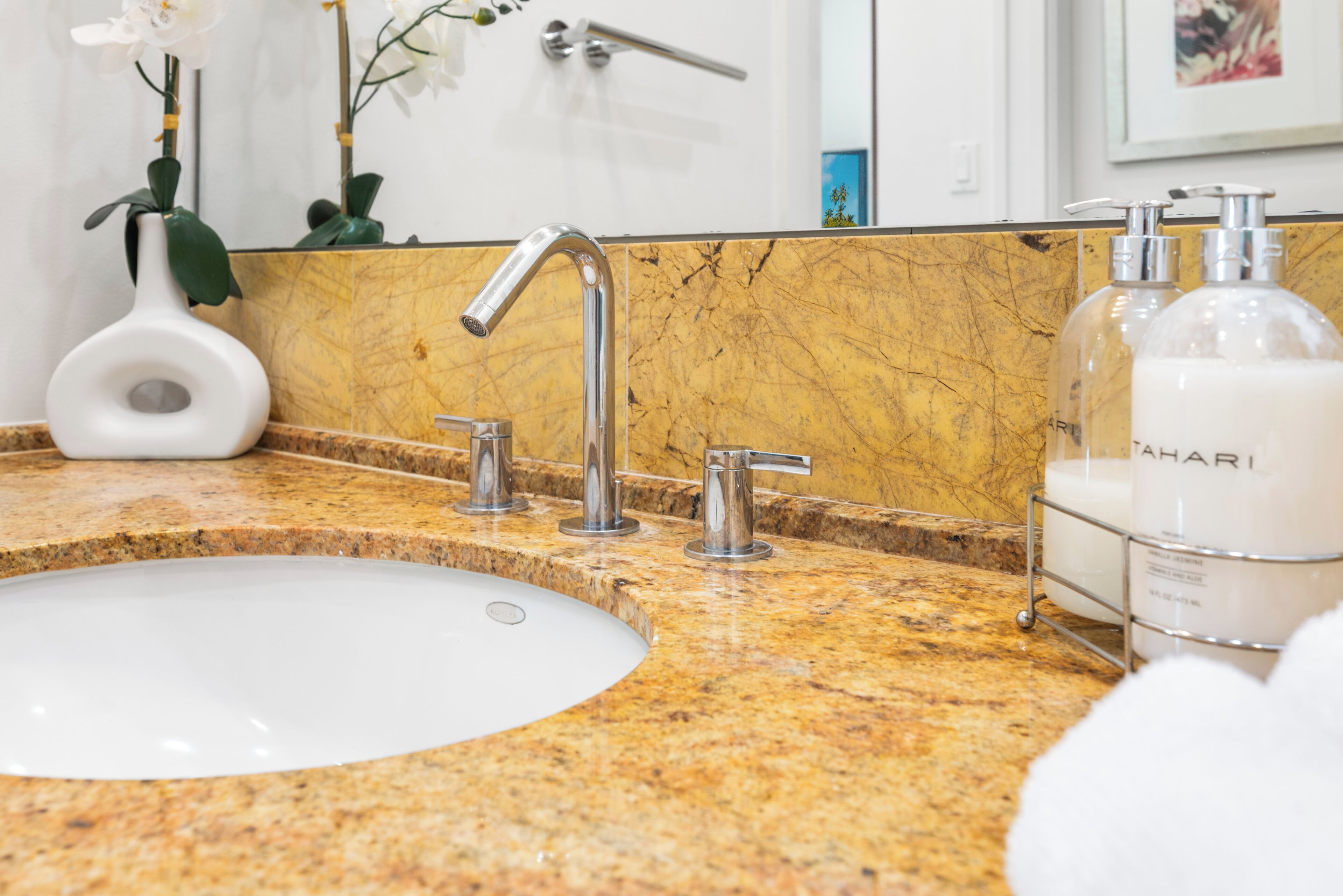 A bathroom with a white sink, a chrome faucet, a marble countertop, and two bottles of lotion.