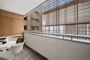 Un balcone moderno con ringhiera bianca, un tavolino con una pianta e vista sulla città attraverso ampie finestre.