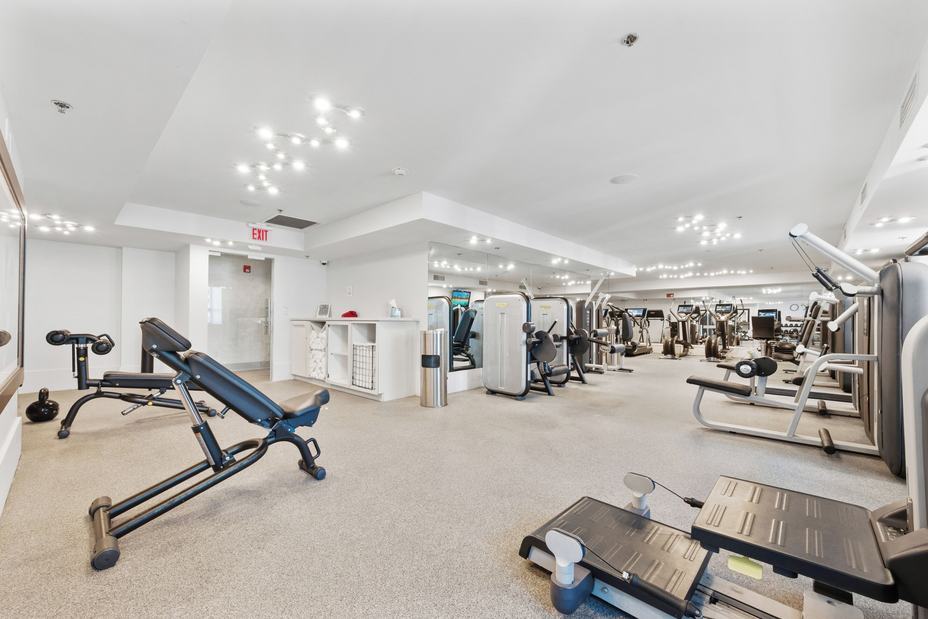 A modern gym with various exercise equipment, a clear exit sign, and a clean, well-lit interior.