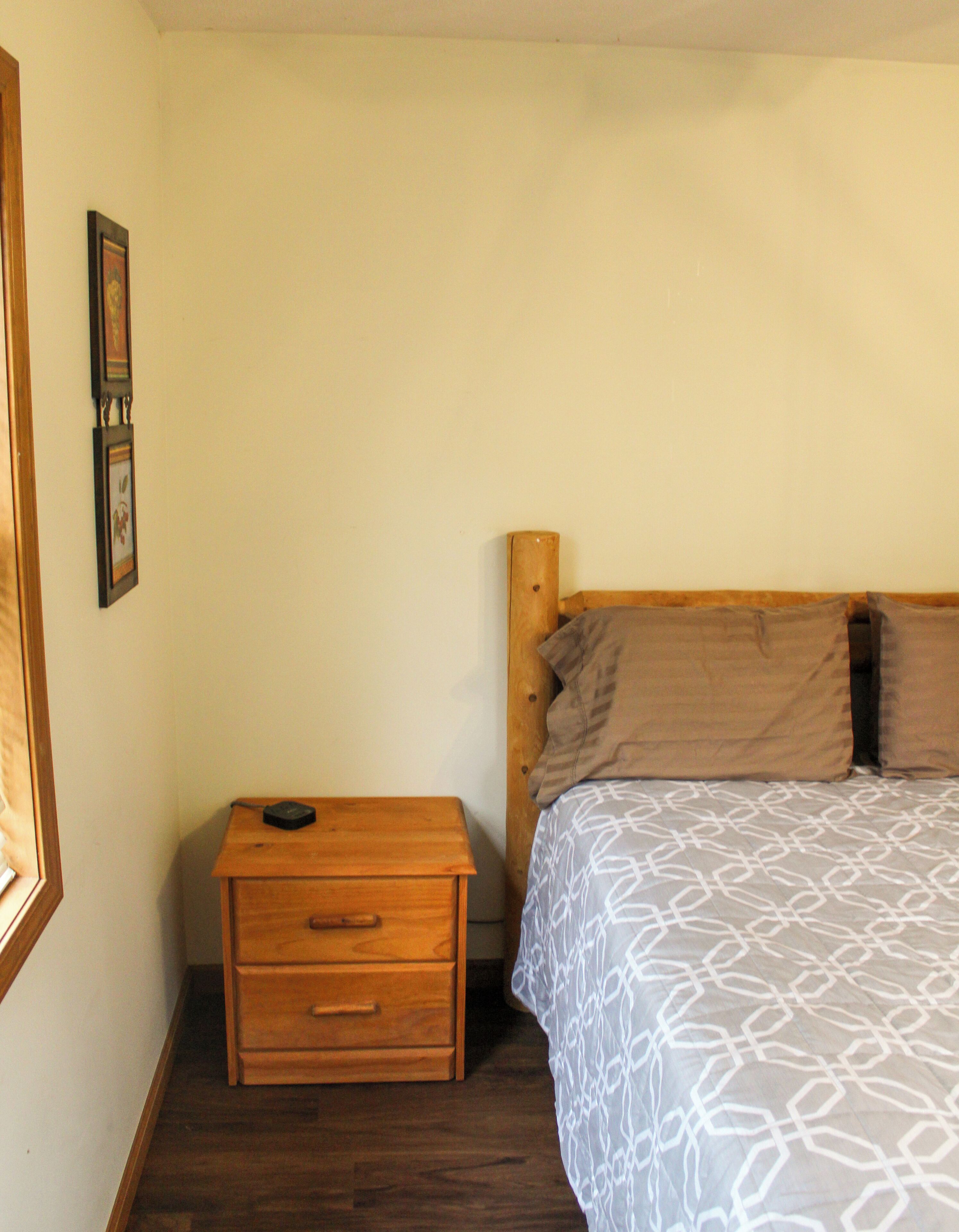 Un dormitorio con una mesita de noche de madera, una cama con ropa de cama estampada y dos cuadros en la pared.