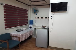 Une cuisine compacte équipée d’un réfrigérateur, d’un distributeur d’eau, d’un ventilateur et d’un téléviseur fixé au mur.