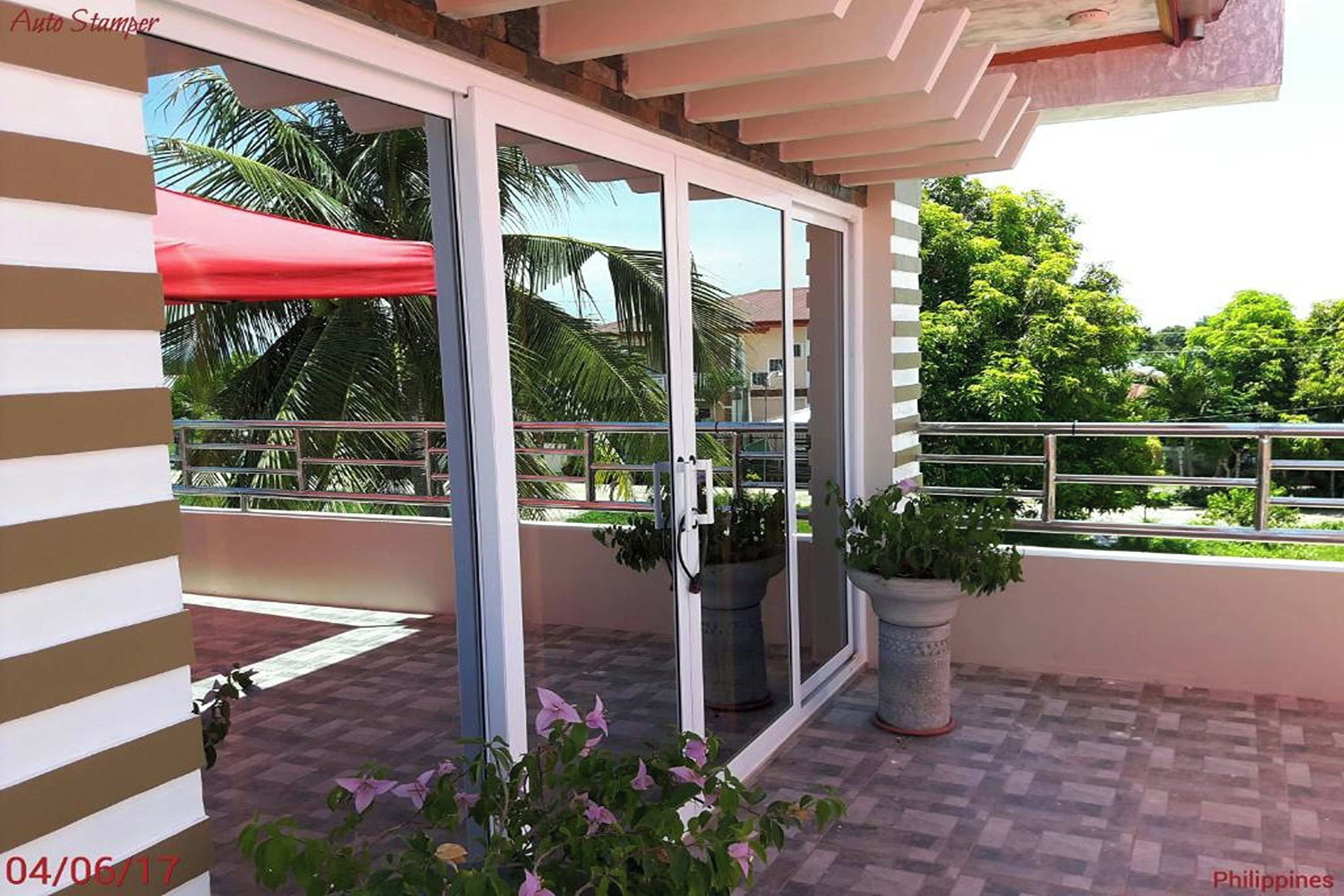 A balcony with a glass door, potted plants, and a red umbrella.