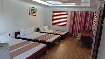 Una camera d'albergo con tre letti singoli, una scrivania, una sedia, una finestra con persiane e un lucernario.