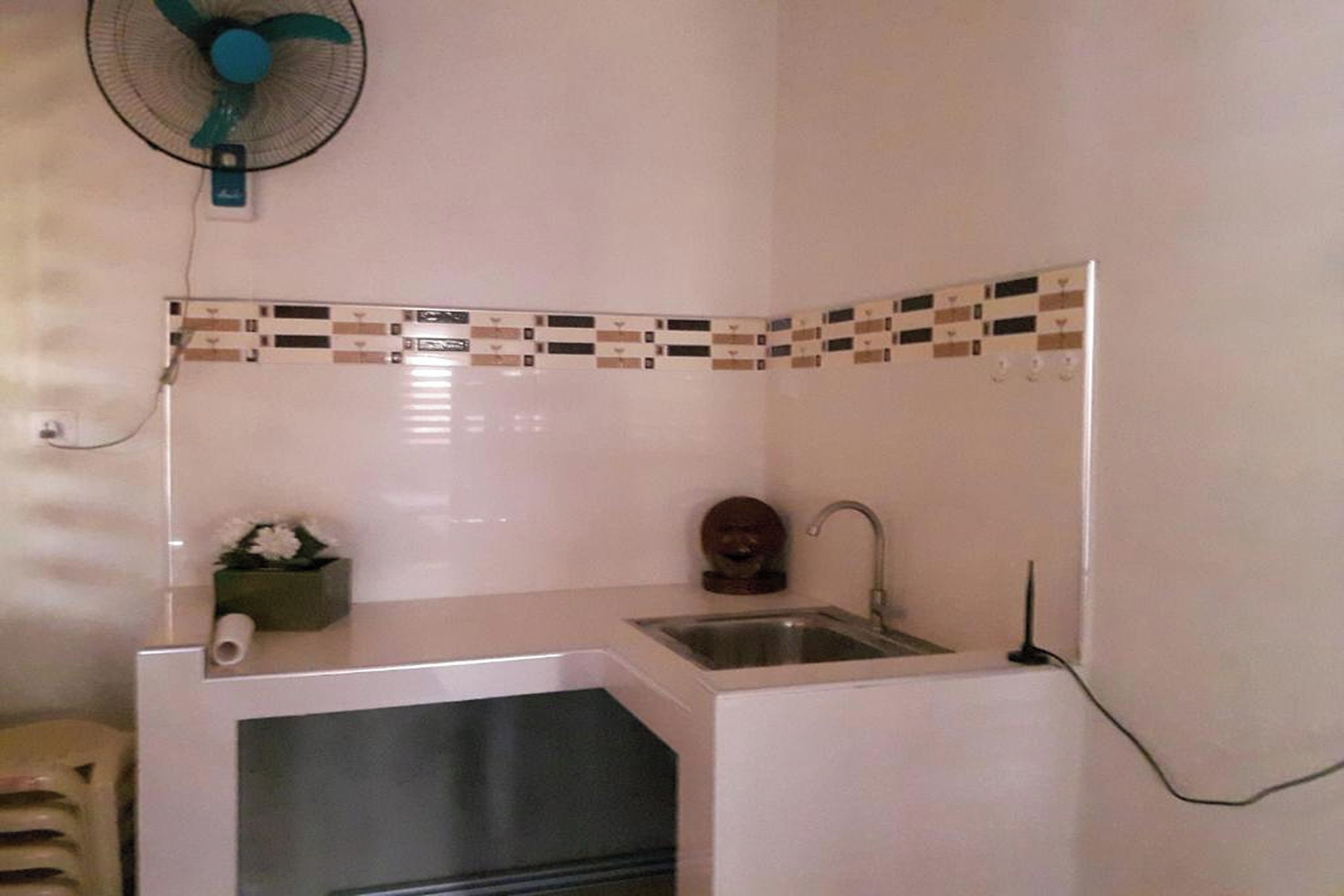 Una cucina compatta con lavandino, ventilatore e decorativa parete rivestita in piastrelle.