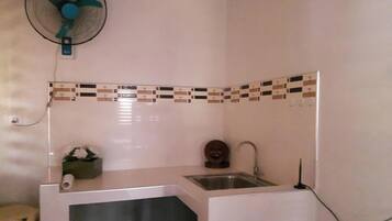 Una cucina compatta con lavandino, ventilatore e decorativa parete rivestita in piastrelle.