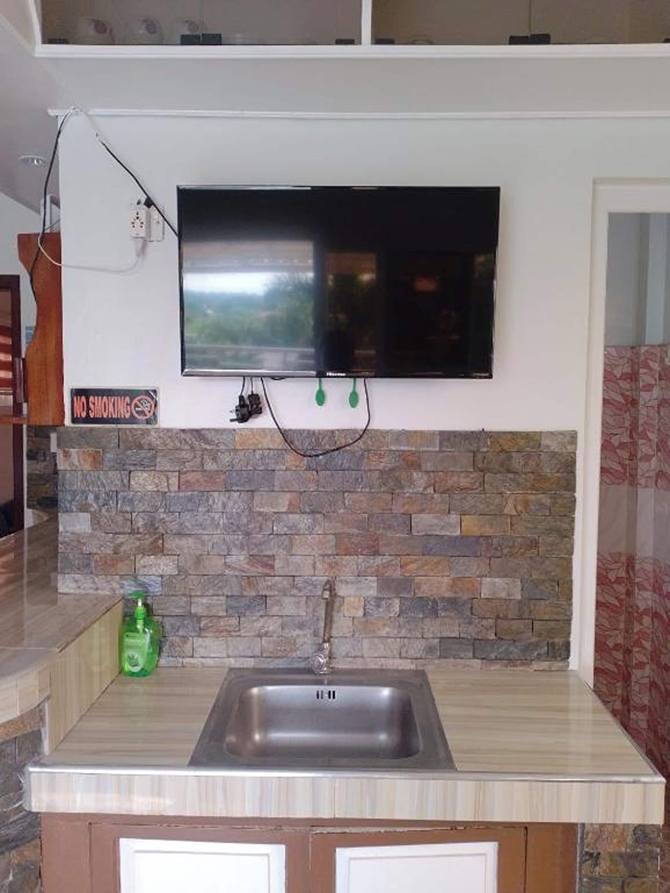 A kitchen with a stone backsplash, a built-in sink, and a flat-screen TV mounted above the counter.