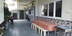 A covered outdoor dining area with a long table and several chairs, a motorcycle parked to the side, and a window with blinds. - Fnt Transient House Near Hundred Islands By Zuzu (Alaminos)