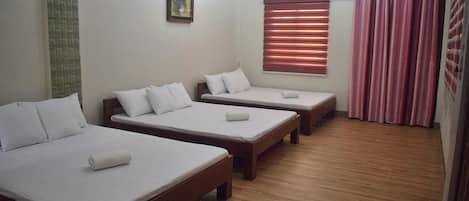 A hotel room with three single beds, a window with blinds, and a skylight.