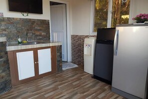 Una cocina con salpicadero de piedra, armarios de madera, un lavamanos de acero inoxidable, un refrigerador y una ventana con vistas a palmeras.