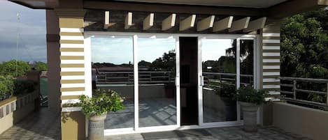 Un espacio exterior cubierto con entrada de vidrio, plantas en macetas y piso de baldosas.