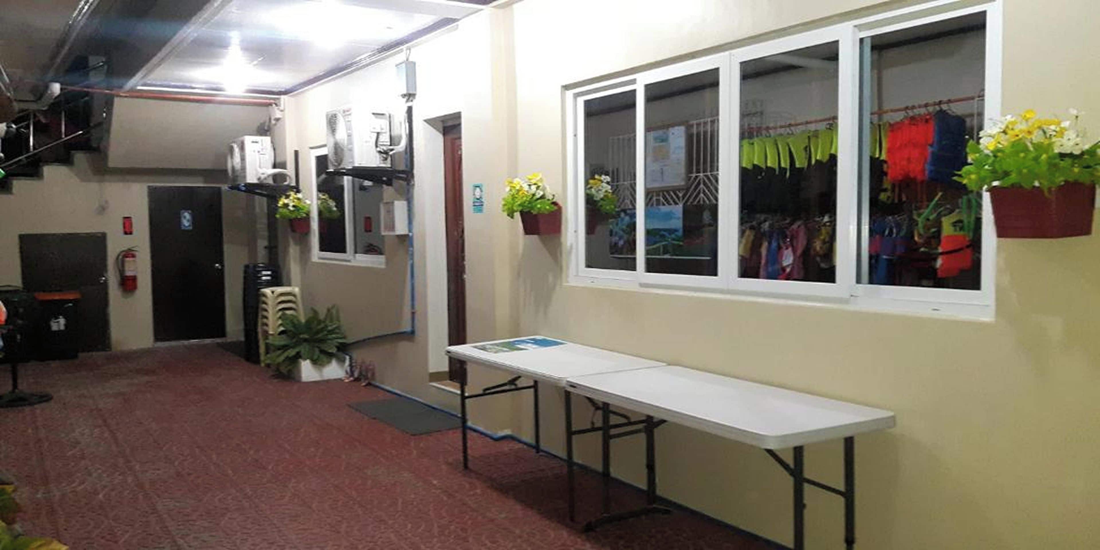 A hallway with a white table, potted plants, and a window with hanging clothes.