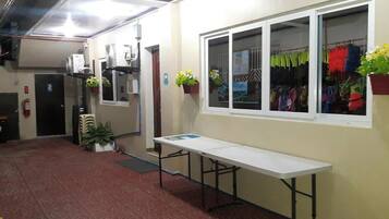 A hallway with a white table, potted plants, and a window with hanging clothes.