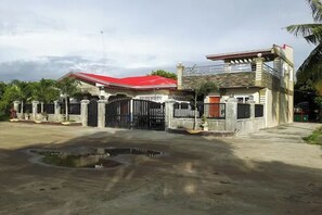 Une maison à deux étages avec un toit rouge, une entrée fermée par un portail et une petite allée.