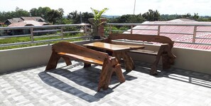 Un balcon avec une table et des bancs en bois, une vue sur les maisons et une rambarde en métal.