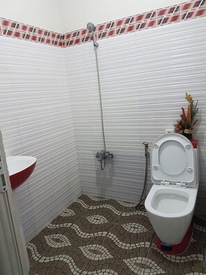 Une petite salle de bain carrelée, équipée d’une douche, de toilettes et d’un lavabo.